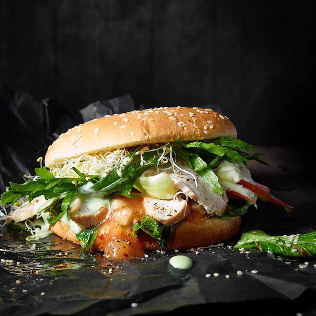 Frisch zubereiteter Chicken Burger Deluxe mit saftigem Hähnchenpatty, knackigem Salat, frischen Toppings und cremiger Sauce in einem goldbraunen Burger Bun serviert.