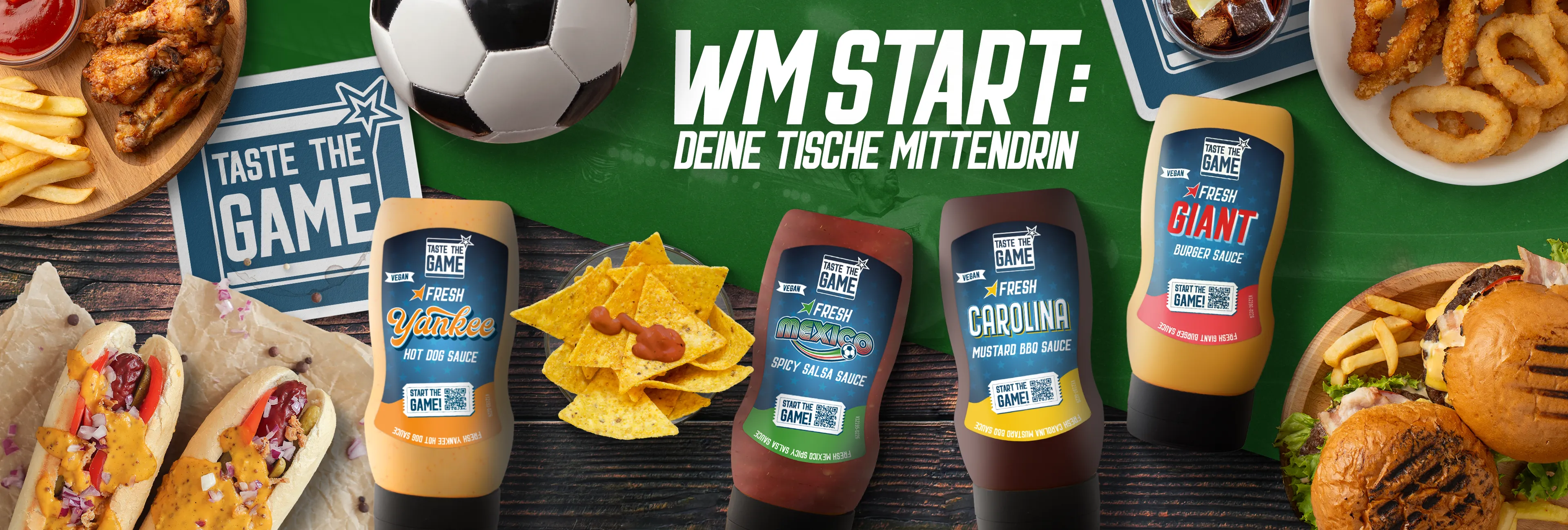 Taste the Game Aktionsbild zur WM mit Burgern, Hot Dogs, Nachos, Pommes und vier veganen Saucenflaschen auf einem Fußballfeld-Hintergrund.