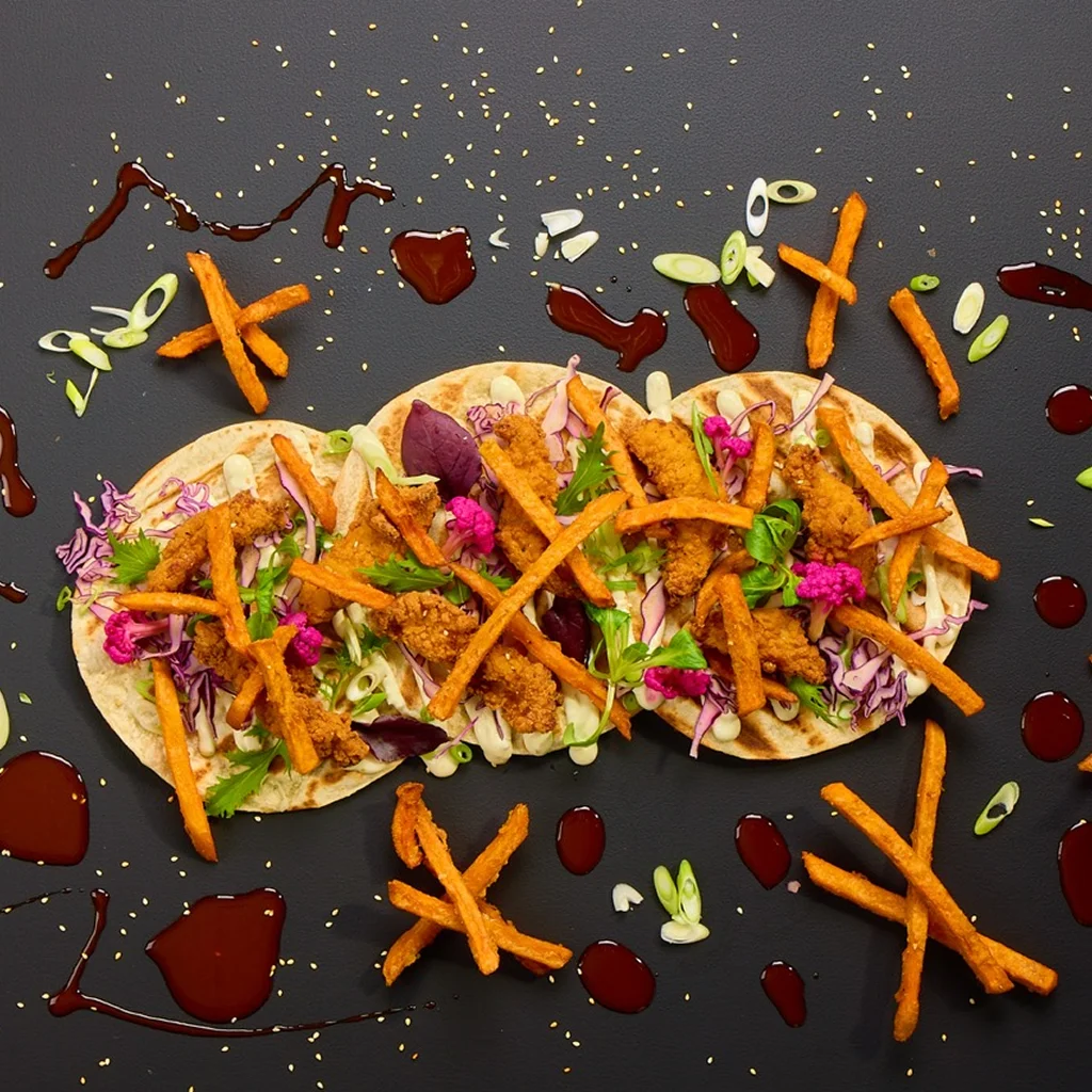 Tortilla-Wrap mit gebackenen Chicken Stripes, Rotkohl, Weißkohl, Süßkartoffelpommes, Jalapeño Lime Dip, Korean Dak Gangjeong Sauce, Frühlingslauch und Sesam.